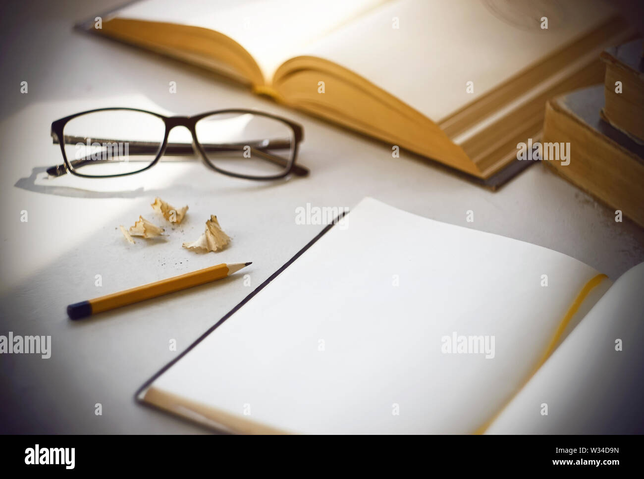 Bright workplace scientist - old shabby books, a diary with a bookmark, glasses in black, yellow pencil and shavings from his sharpening. Stock Photo