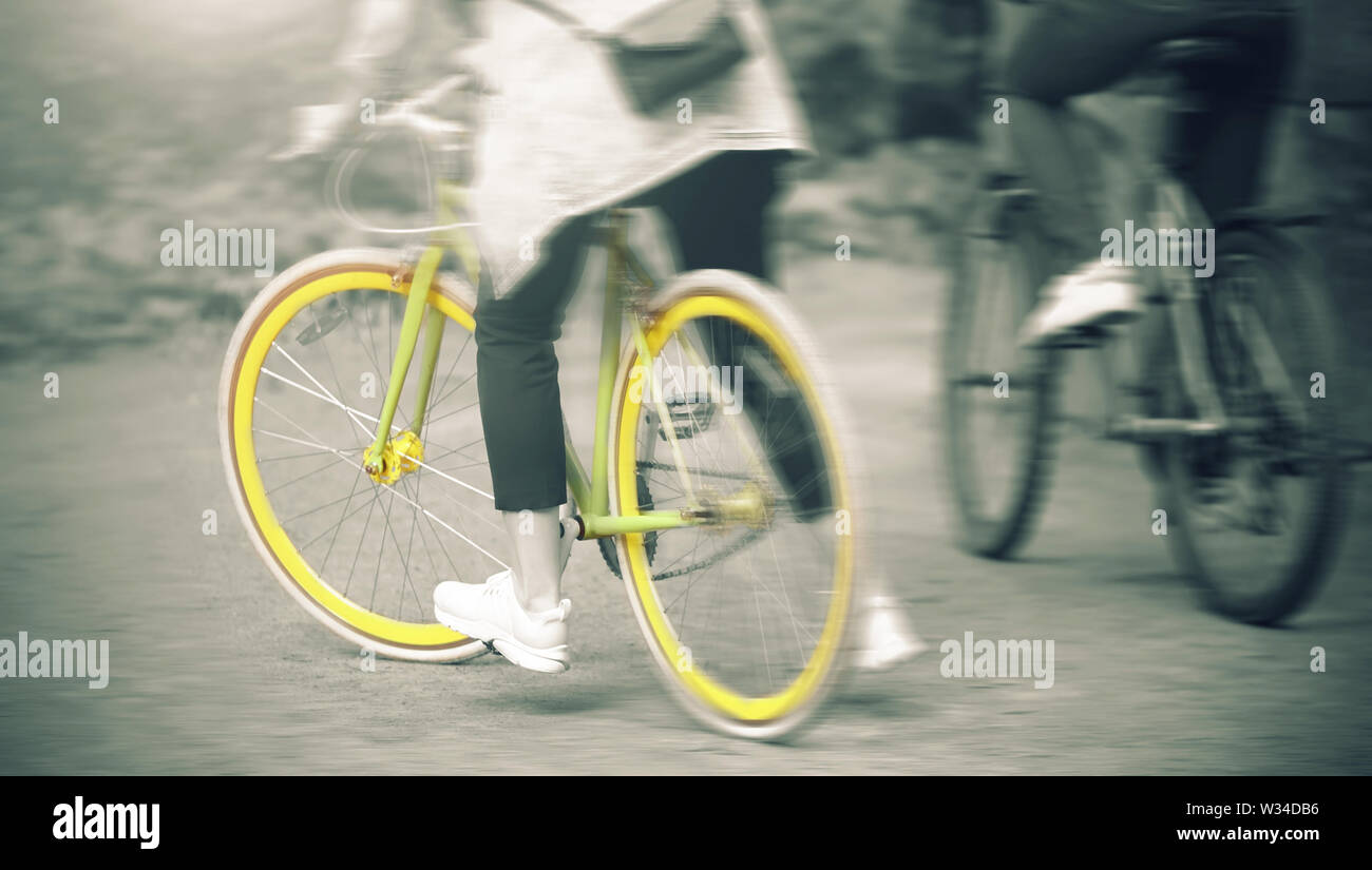 A girl and a guy together quickly ride on sports bikes in the Park on a summer day. The image is in a monochrome filter, and the girl's bike is yellow Stock Photo