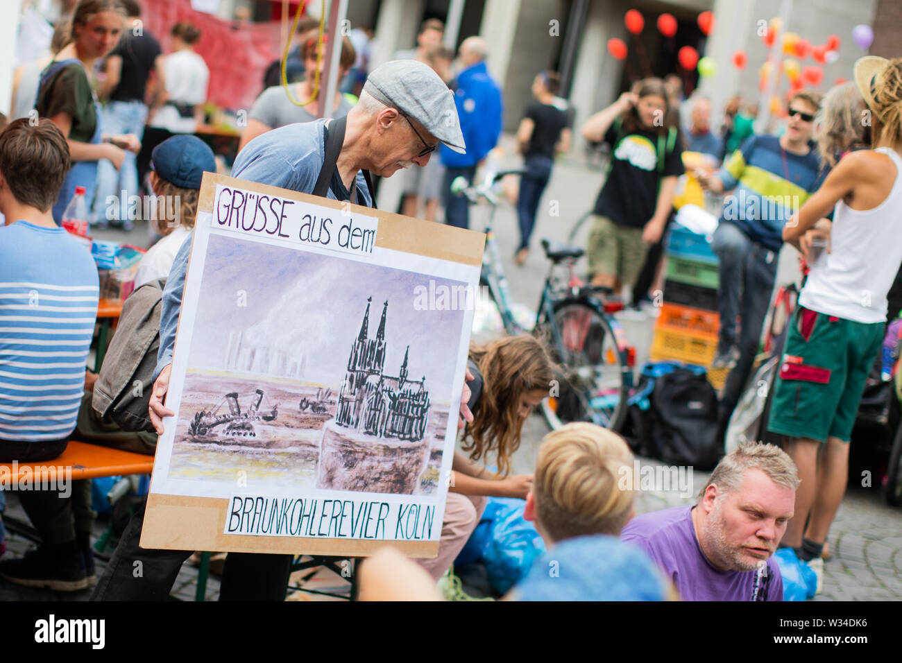 Cologne, Germany. 12th July, 2019. Reinhard (73), a retired teacher, takes part in the closing rally of a Fridays for Future demonstration at the Alter Markt in the Old Town with a poster showing Cologne Cathedral in the brown coal district. Climate protectors from 'Fridays for Future' had demonstrated here non-stop for five days. Credit: Rolf Vennenbernd/dpa/Alamy Live News Stock Photo