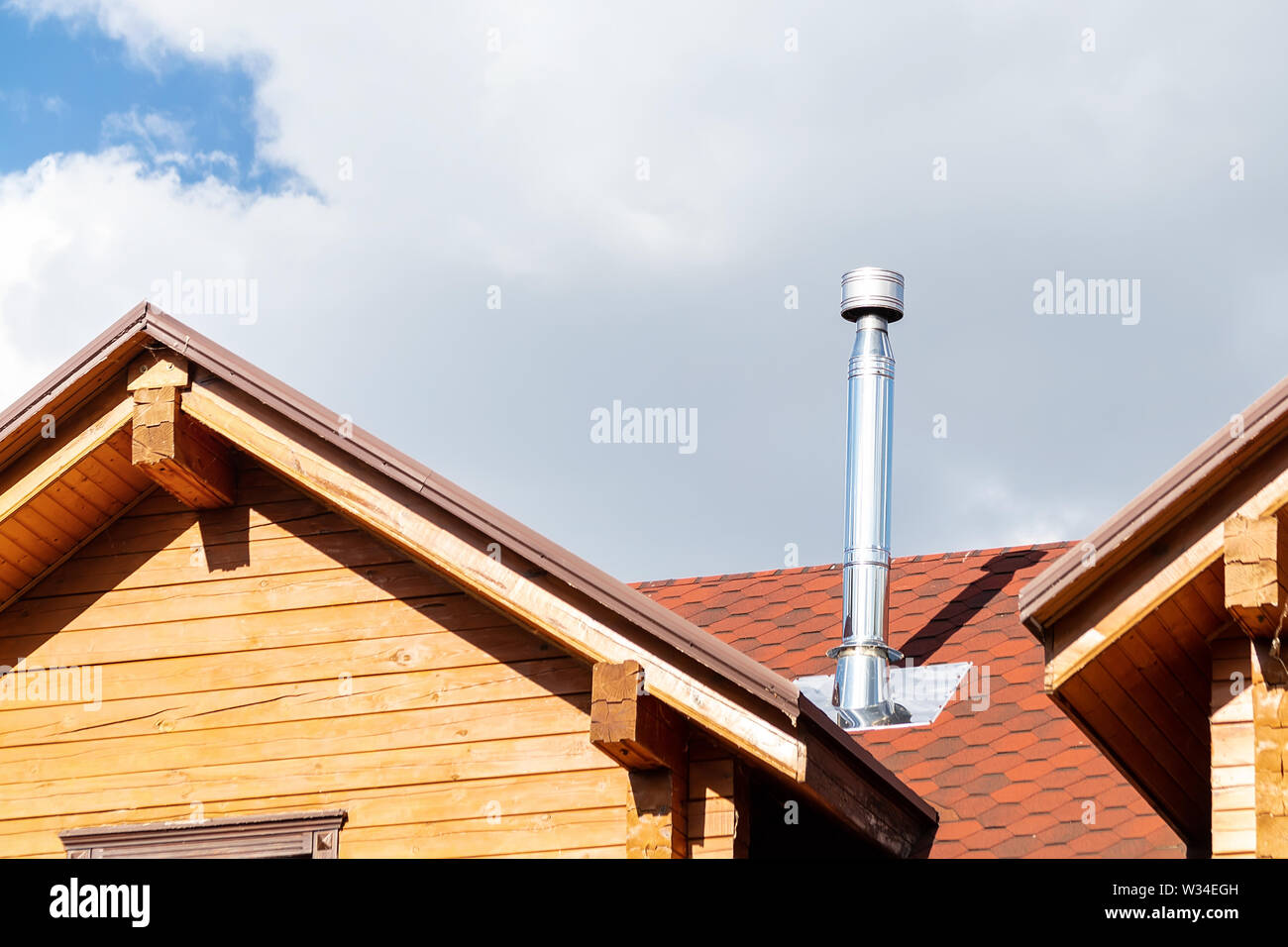 Stainless steel chimney pipe on roof of modern wooden beam cottage