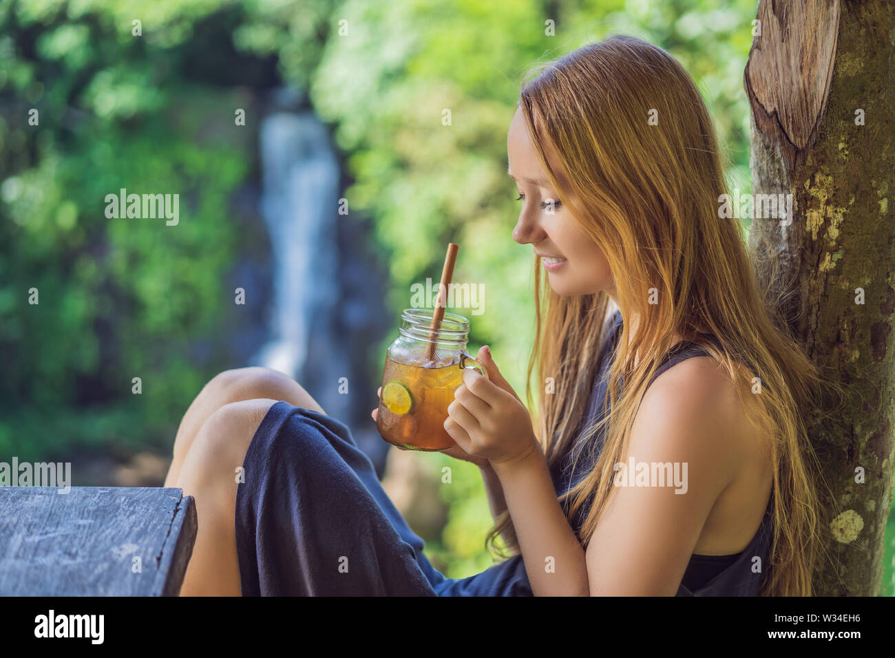 Closeup portrait image of a beautiful woman drinking ice tea with feeling happy in green nature and waterfall background Stock Photo - Alamy