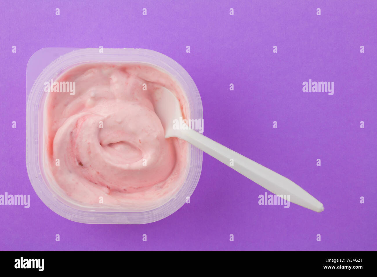 Yogurt cup with strawberry yogurt and with white plastic spoon dipped isolated on purple background - top view photo with space for text Stock Photo