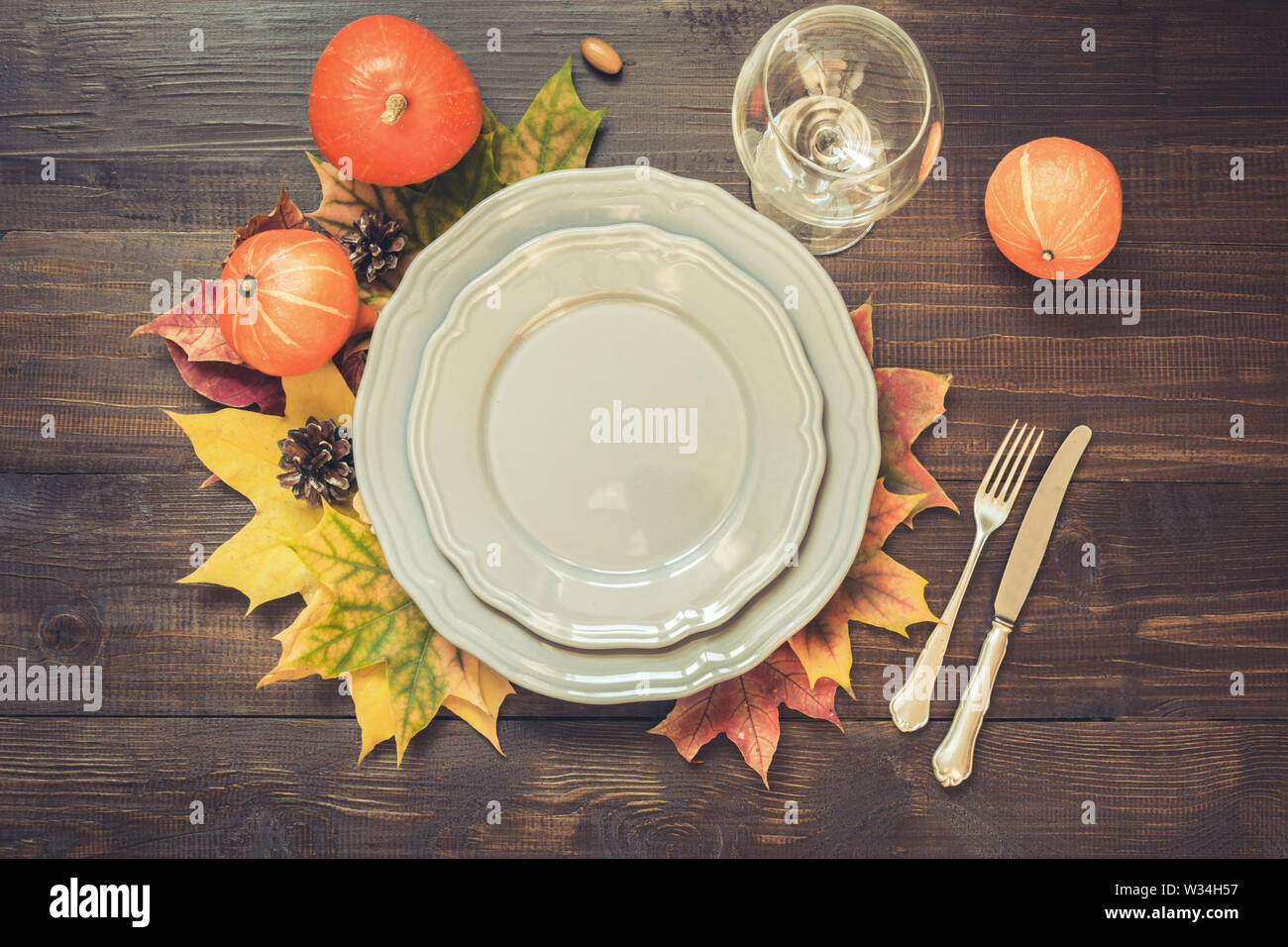 Autumn and Thanksgiving day table setting with fallen leaves, grey dish and silverware on wooden table. Top view. Stock Photo
