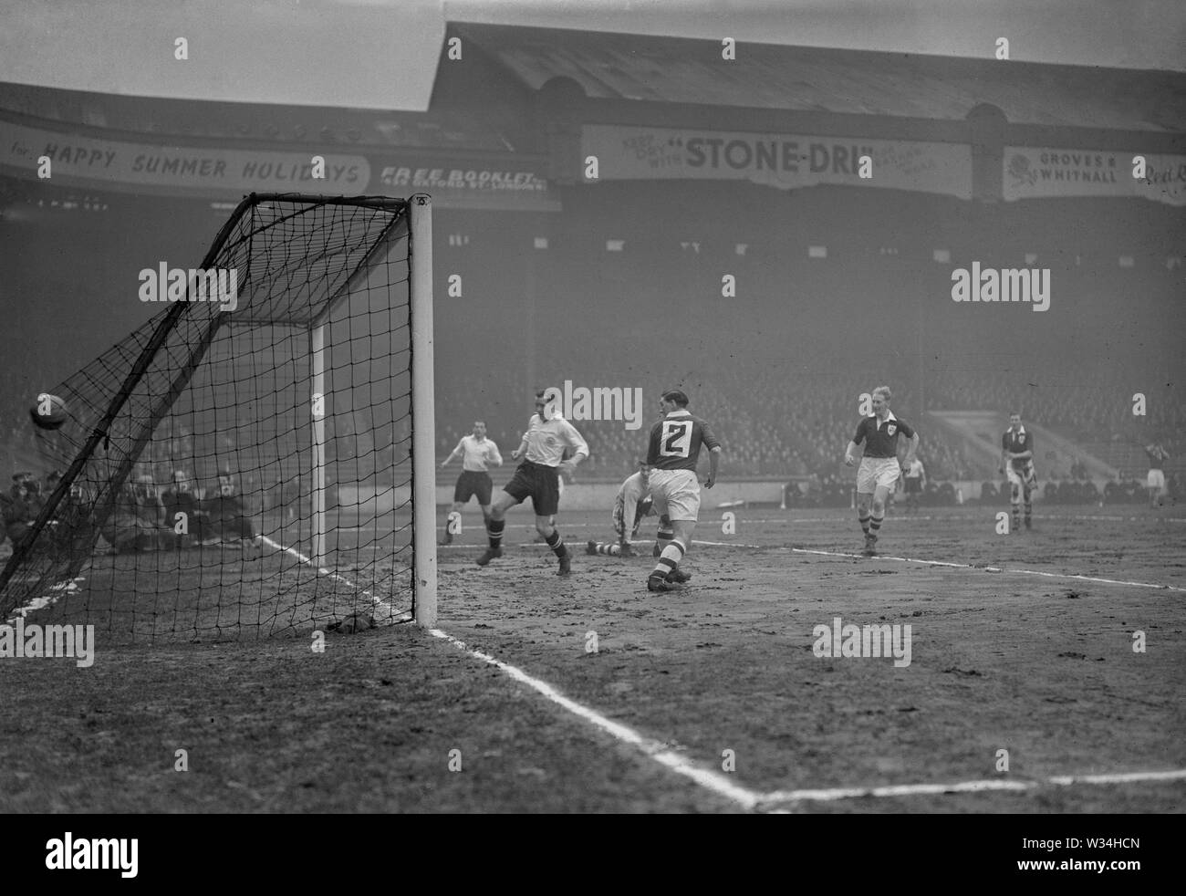 England centre-half Nat Lofthouse (white shirt, nearest camera) and League of Ireland full-back M. Burke (no.2) watch the ball enter the net for a goal. Ireland goalkeeper D. Barrett is down on one knee. The match as held at Maine Road in Manchester. Stock Photo