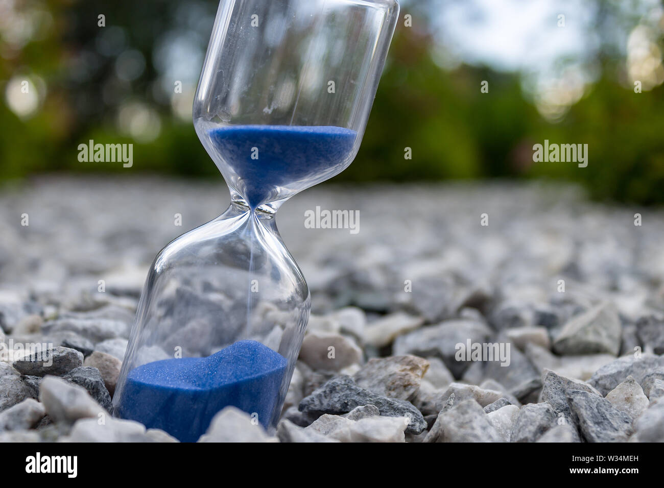 Hourglass with beautiful blue sand lie on small stones Stock Photo