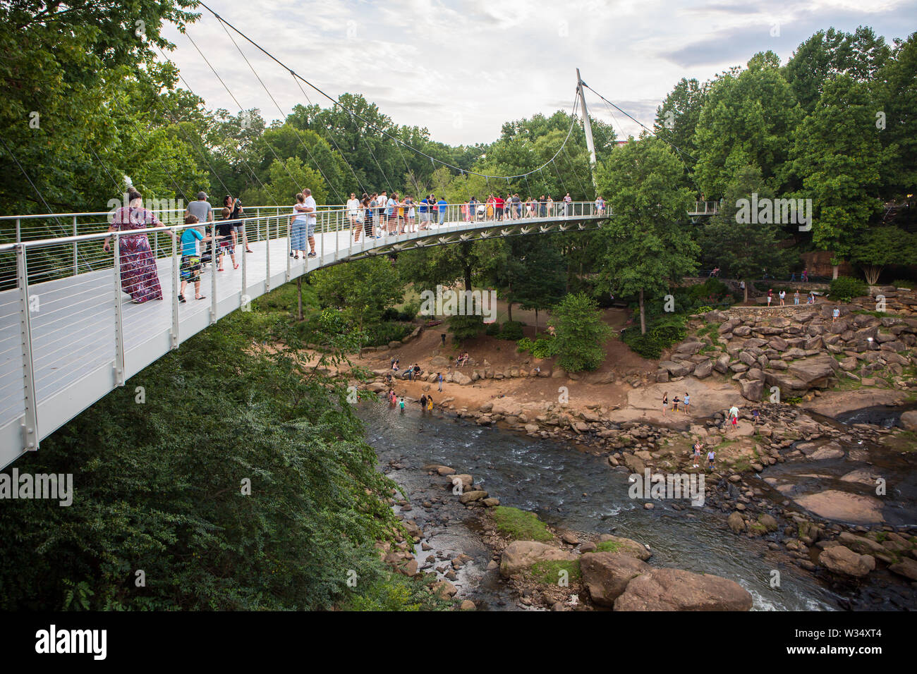 GREENVILLE, SC (USA) - July 5, 2019: Visitors to Falls Park linger on Liberty Bridge overlooking the Reedy River waterfalls. Stock Photo