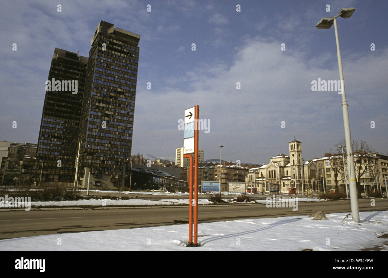 2nd April 1993 During the Siege of Sarajevo: the view across 'Sniper Alley' (Zmaja od Bosne) from the front of the Assembly Building. On the right is Saint Joseph’s Church (Roman Catholic); on the left, the twin Unis Towers. Behind the signpost in the centre is the Dr Abdulah Nakas General Hospital, known locally as the 'City' or 'French' Hospital during the war. Stock Photo