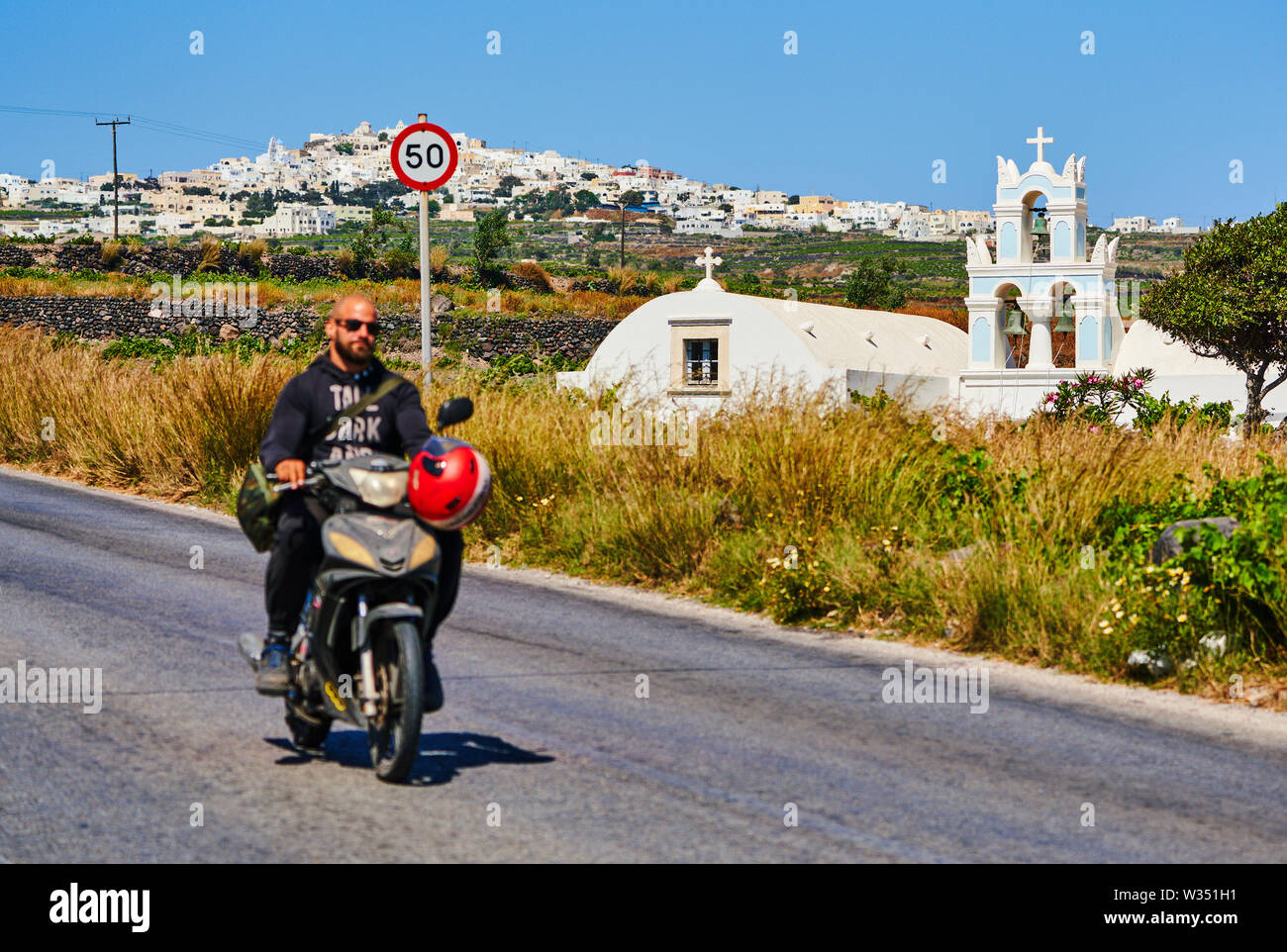Tourist on a motorbike without helmet passing a Church in Megalochori near Oia and Fira, Santorini , Greece at 02.06.2019. © Peter Schatz / Alamy Stoc Stock Photo
