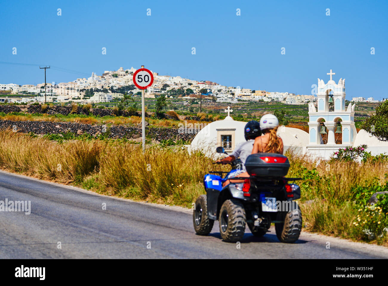 Tourists on a quad motorbike with helmets passing a Church in Megalochori near Oia and Fira, Santorini , Greece at 02.06.2019. © Peter Schatz / Alamy Stock Photo