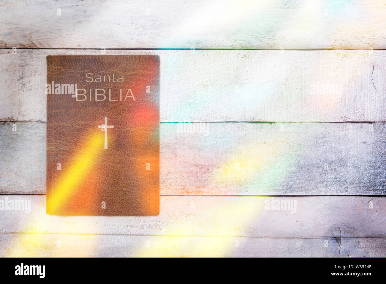 Spanish version of Holy Bible with some stained glass reflection on a wooden table. Top view and empty copy space for Editor's text. Stock Photo
