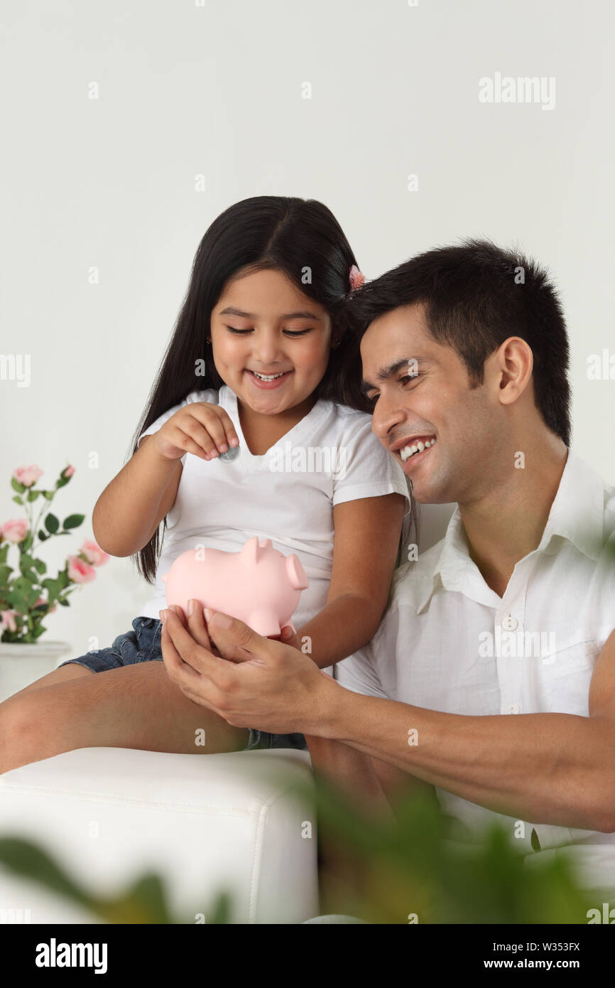 Indian girl putting coin into a piggy bank with her father Stock Photo ...