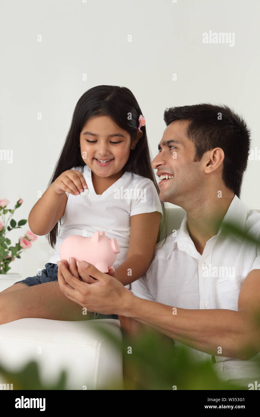 Girl putting coin into a piggy bank with her father Stock Photo - Alamy