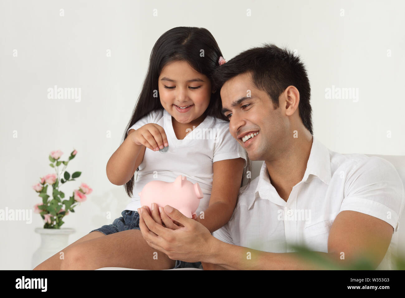 Girl putting coin into a piggy bank with her father Stock Photo - Alamy