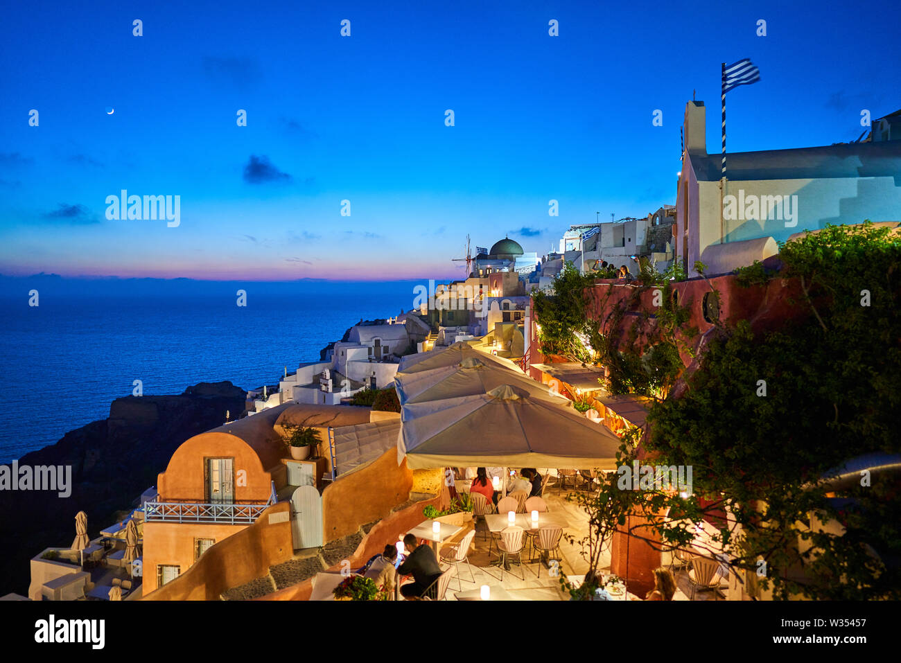 Tourists in luxury restaurants and on Oia Castle wait for the sunset with Caldera View and the famous Windmill in Oia, Santorini , Greece at 04 June 2 Stock Photo