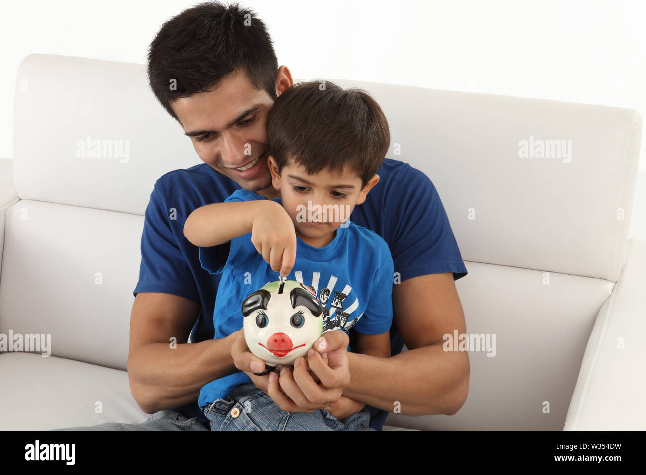Boy putting coin into a piggy bank with his father Stock Photo - Alamy
