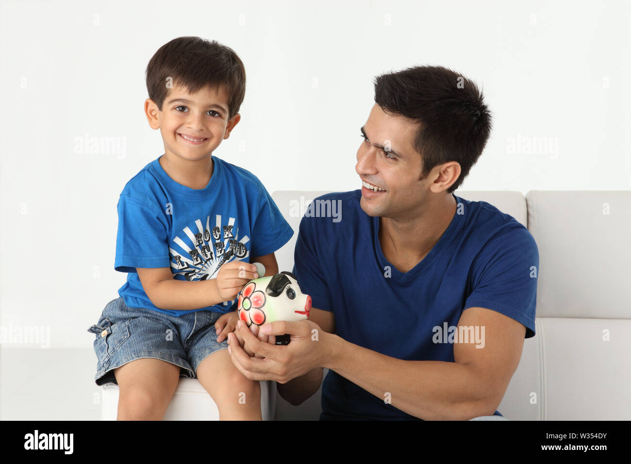 Boy putting coin into a piggy bank with his father Stock Photo - Alamy