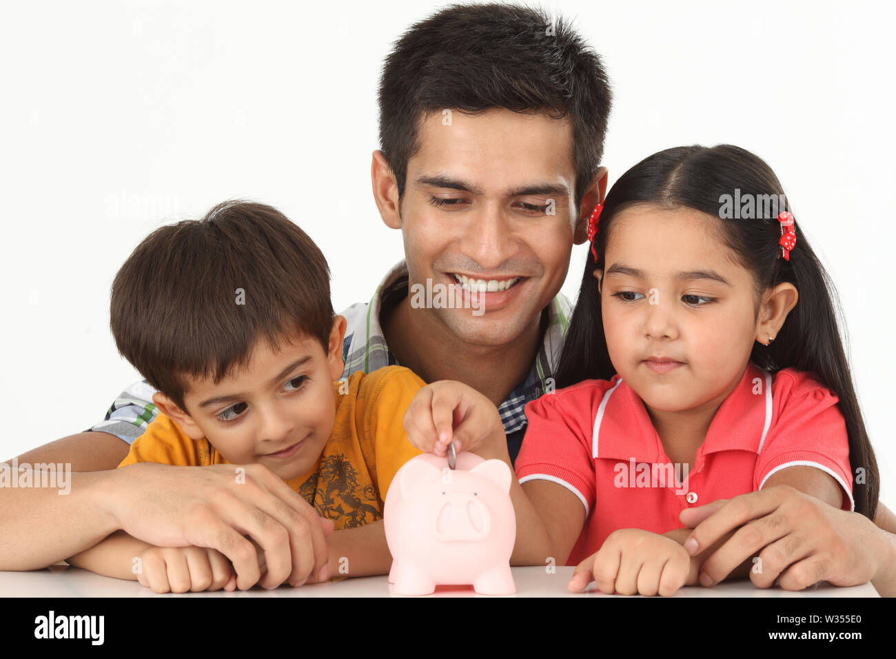 Indian girl putting coin into a piggy bank with her father and brother ...