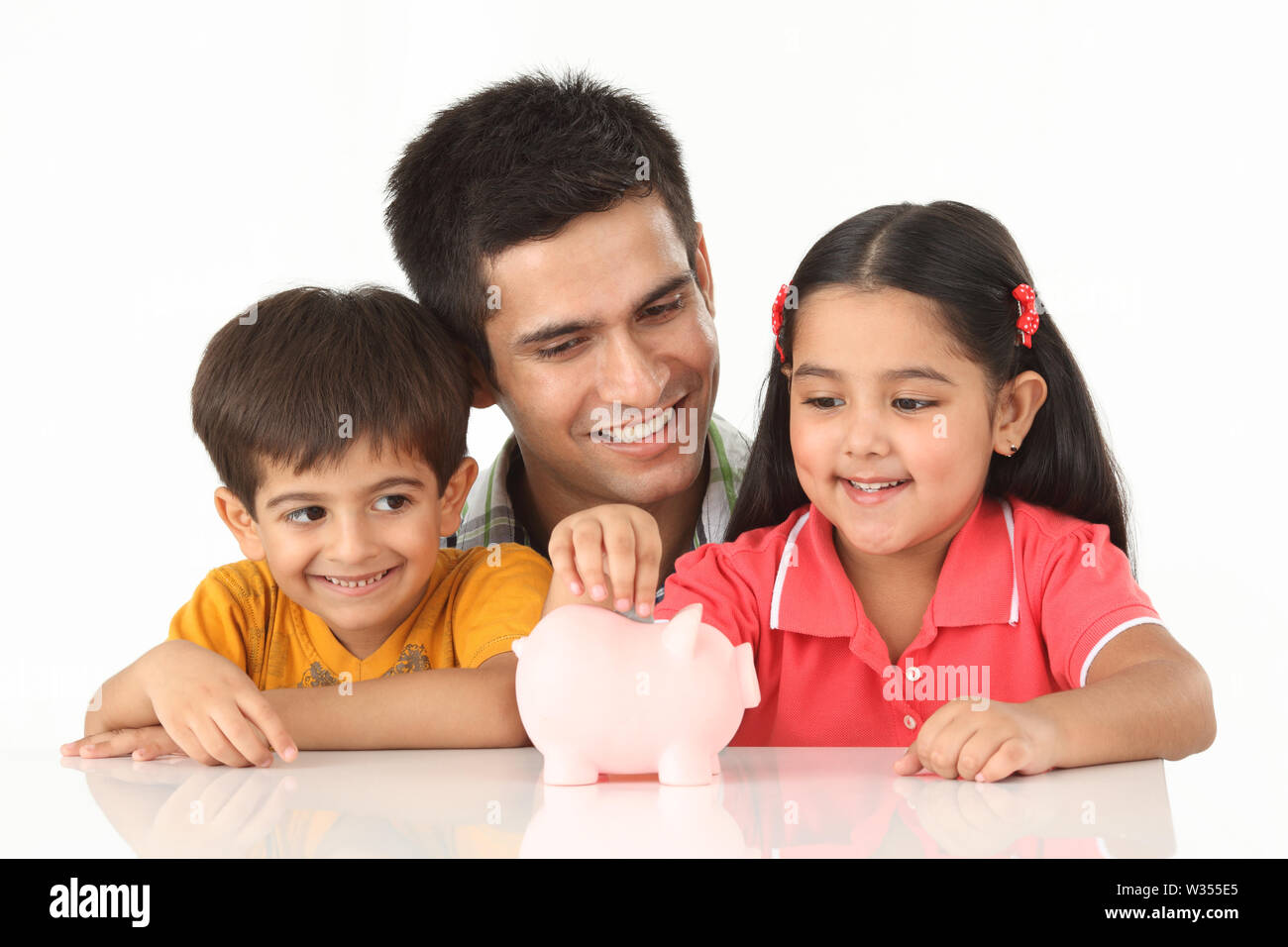 Girl putting coin into a piggy bank with her father and brother Stock ...