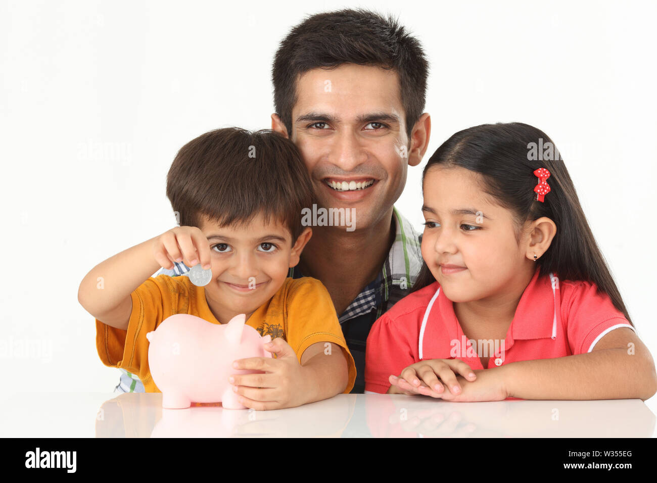 Boy putting coin into a piggy bank with his father and sister Stock ...