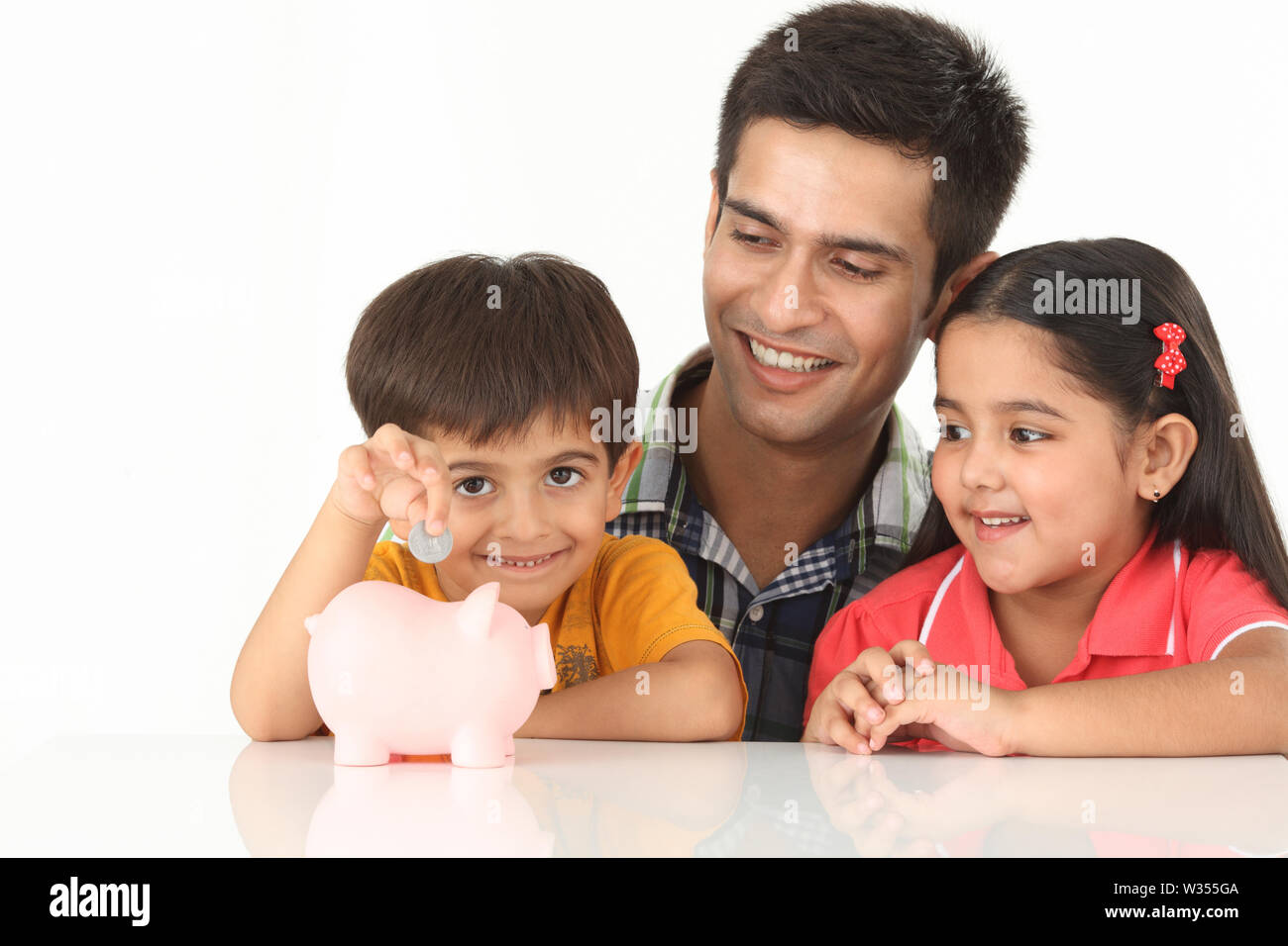 Boy putting coin into a piggy bank with his father and sister Stock ...