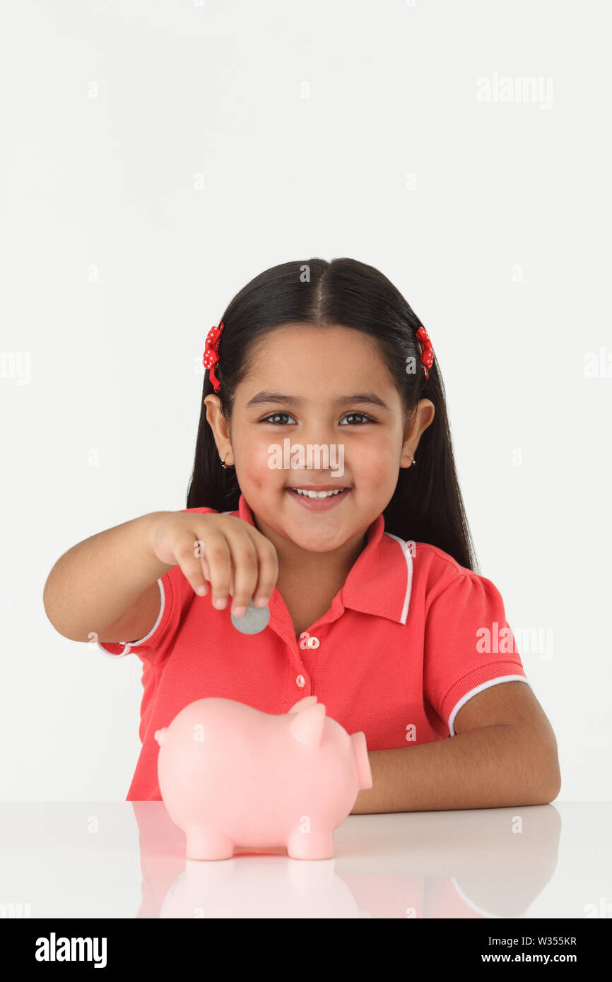 Girl inserting coin into a piggy bank and smiling Stock Photo - Alamy