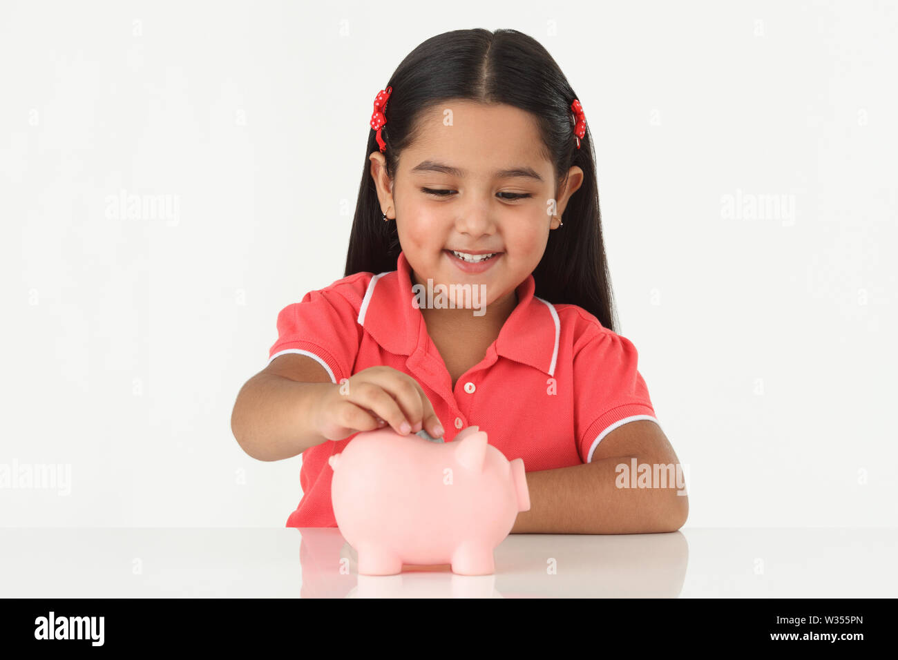 Girl inserting coin into a piggy bank and smiling Stock Photo - Alamy