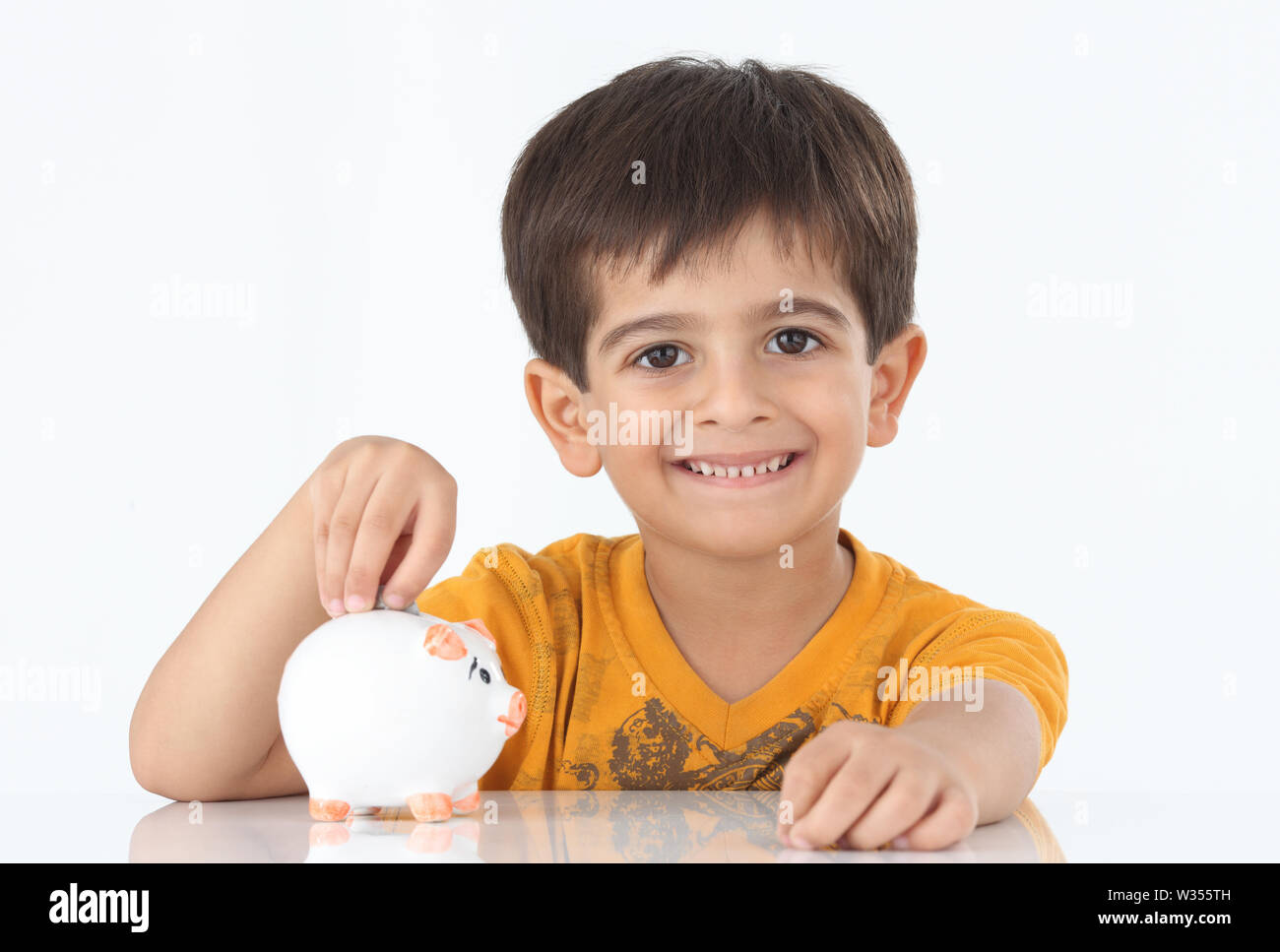 Boy inserting coin into a piggy bank and smiling Stock Photo - Alamy