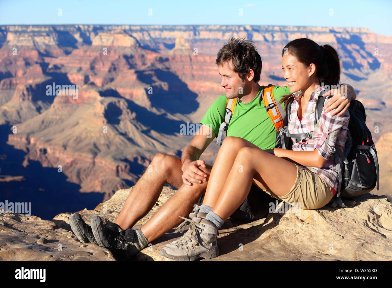 Hiking couple portrait - hikers in Grand Canyon enjoying view of nature landscape smiling happy. Young couple trekking, relaxing after hike on south rim of Grand Canyon, Arizona, USA. Man and woman. Stock Photo