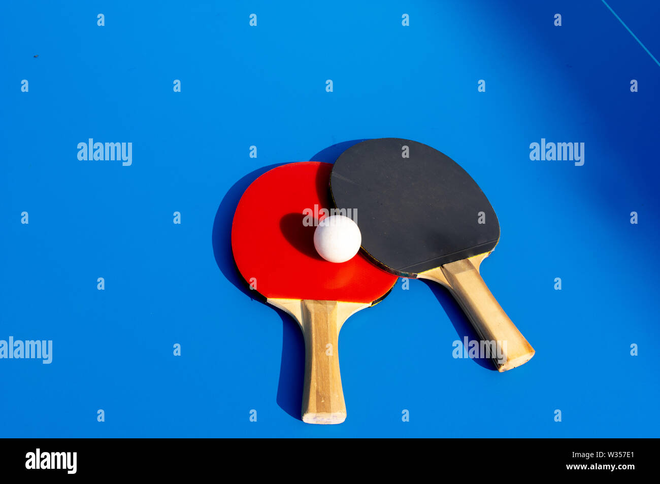 close up shot of two table tennis paddles with a ball on blue table Stock Photo