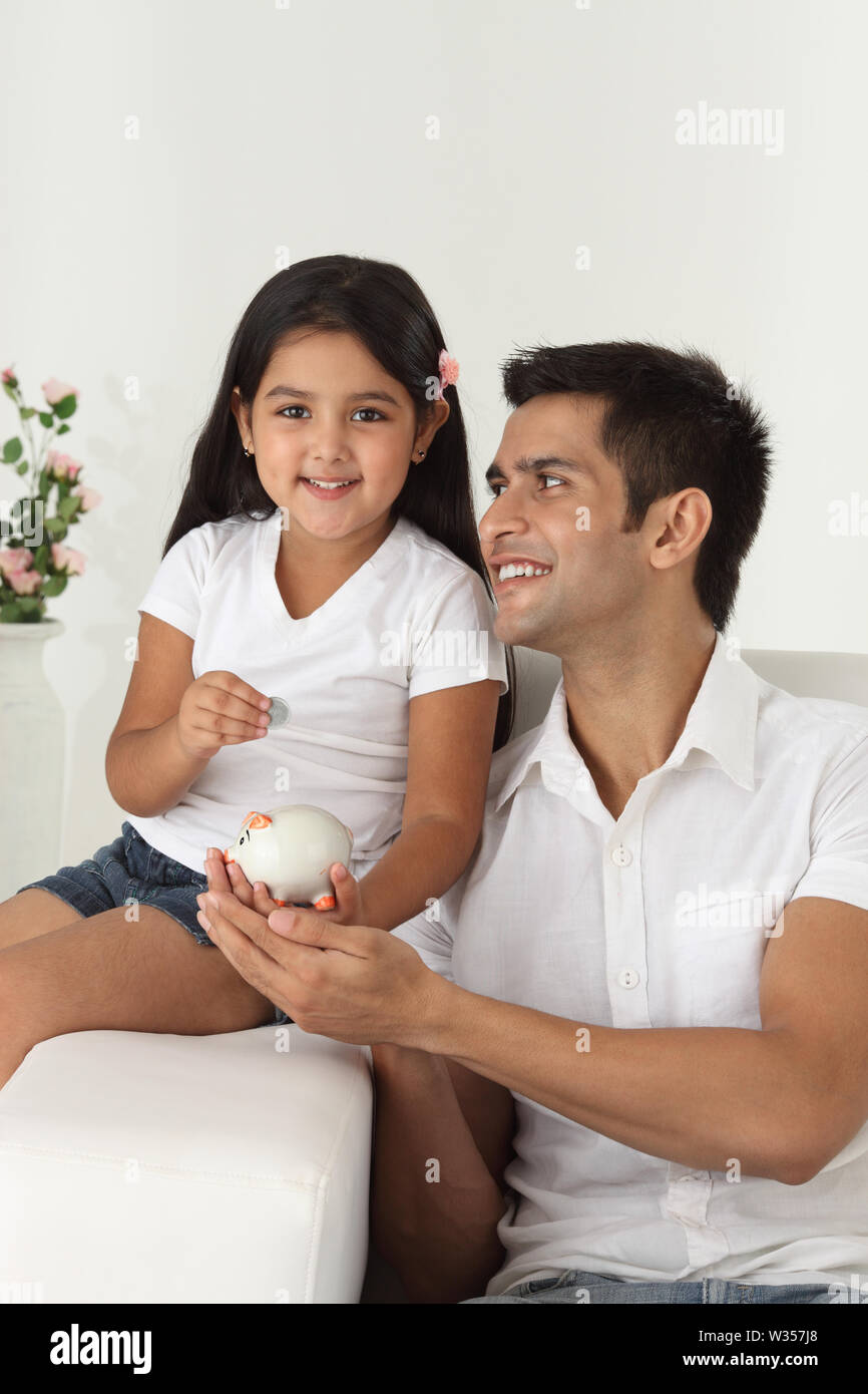 Girl putting coin into a piggy bank with her father Stock Photo - Alamy