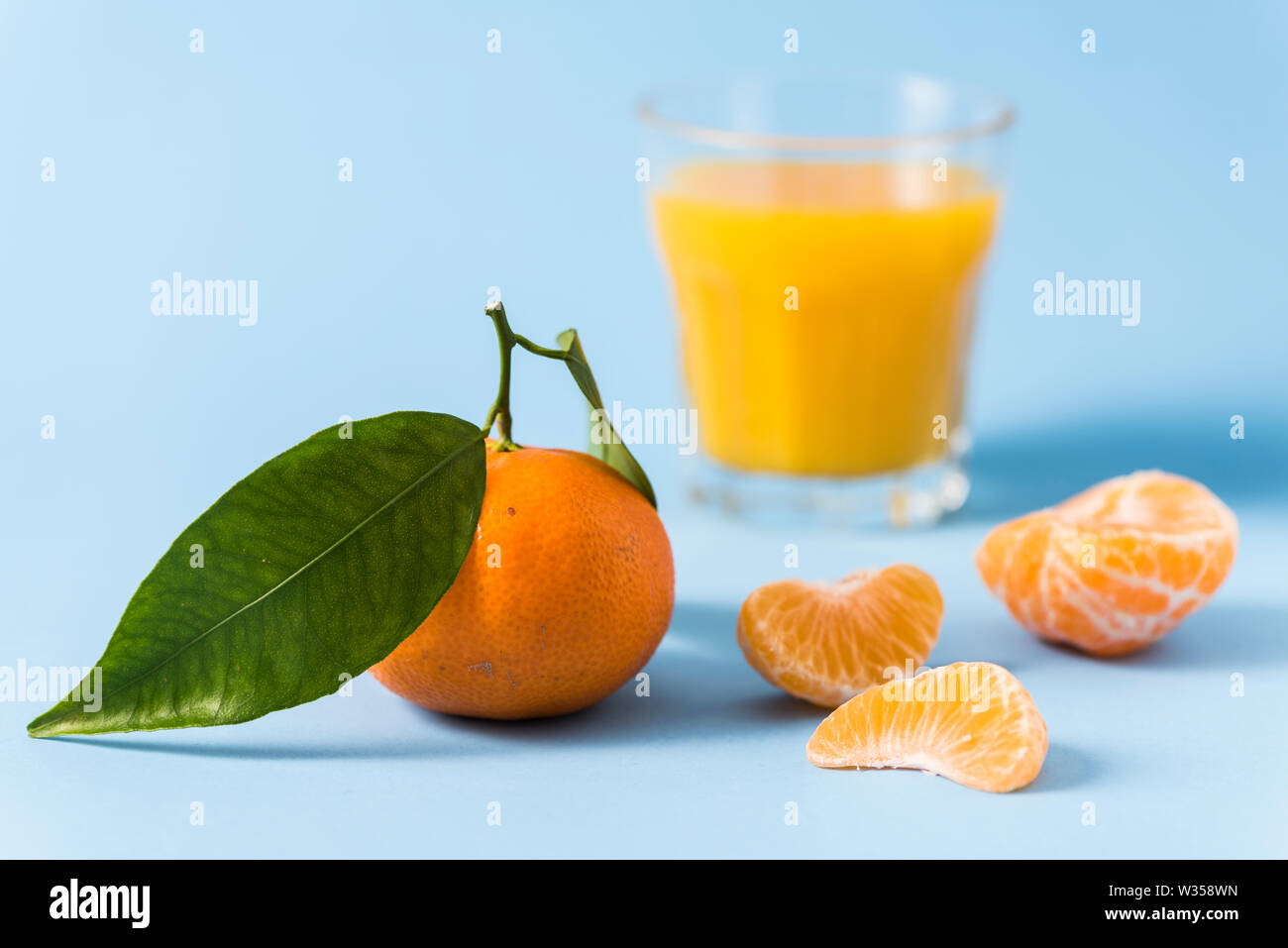 Leafy clementine, peeled clementine and glass of clementine juice on a pale blue background Stock Photo