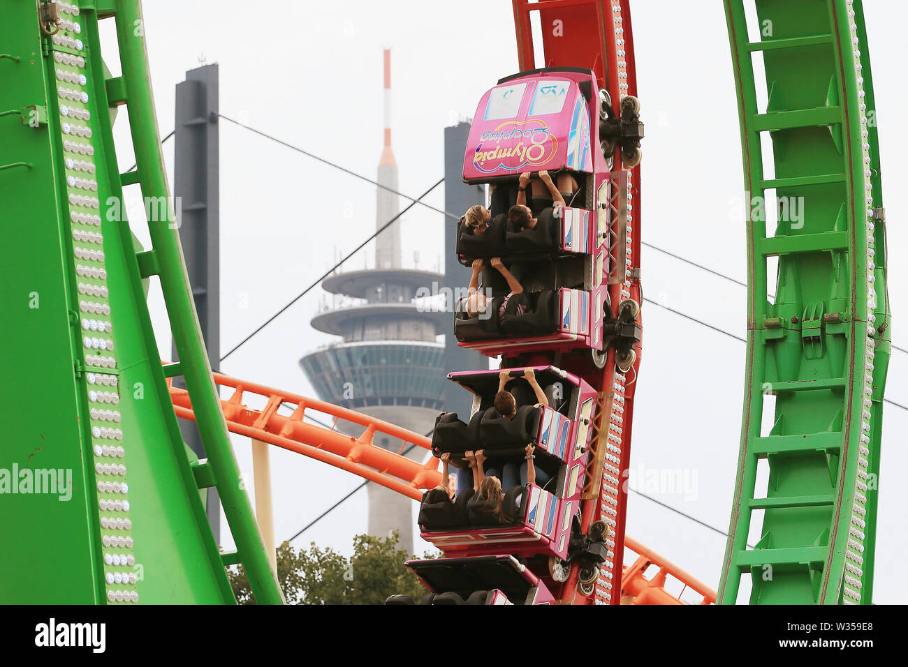 Duesseldorf, Germany. 12th July, 2019. Passengers into the Olympia Looping ride at the beginning of the biggest fair on the Rhine. In the background the Rhine tower and pillar of the Rhine knee bridge can be seen. Several million visitors are expected by 21 July. Credit: David Young/dpa/Alamy Live News Stock Photo