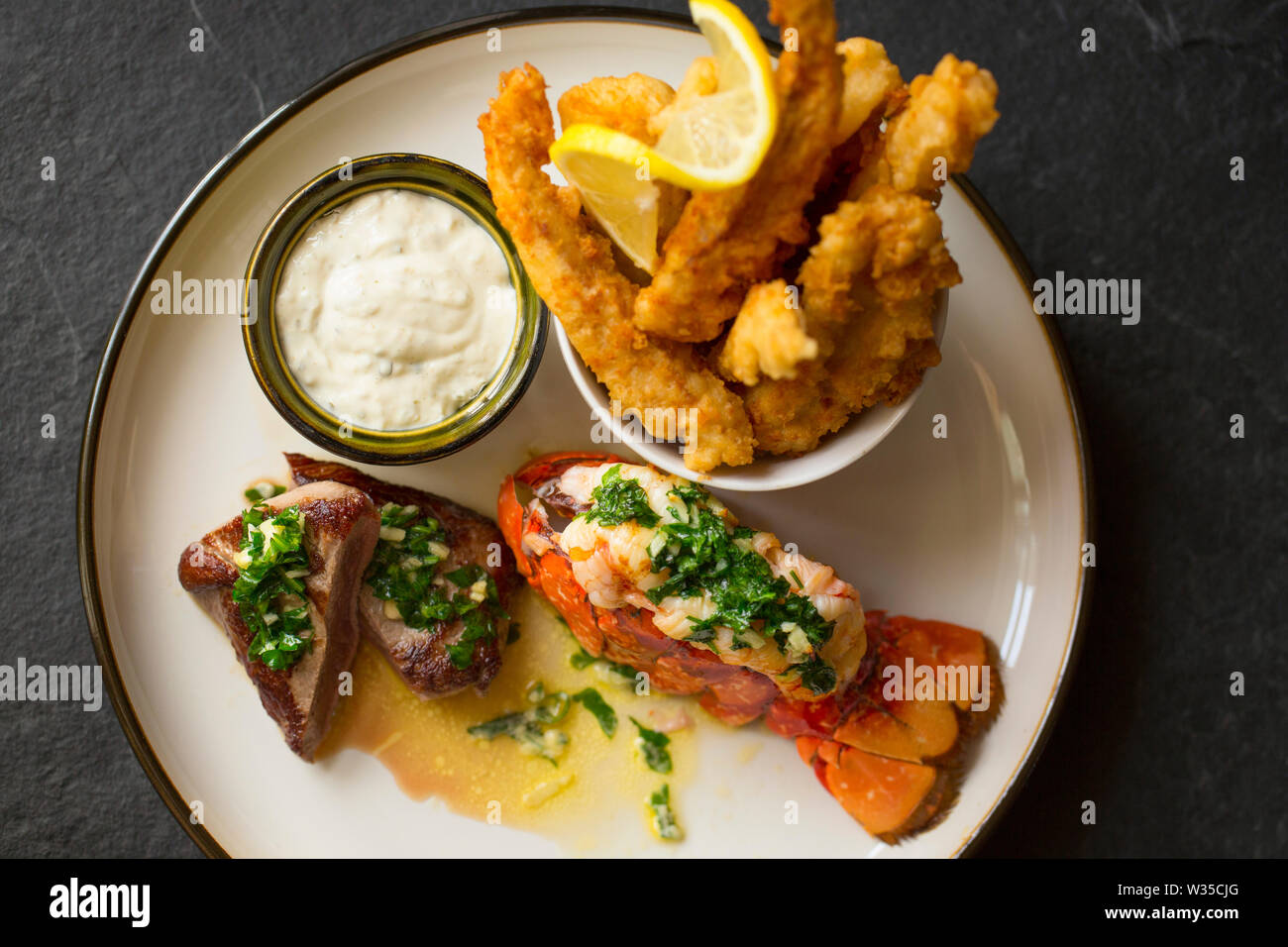 A homemade dish of surf and turf. It features a lobster tail that has been grilled, and a flash fried roe deer saddle fillet that have both had a garl Stock Photo