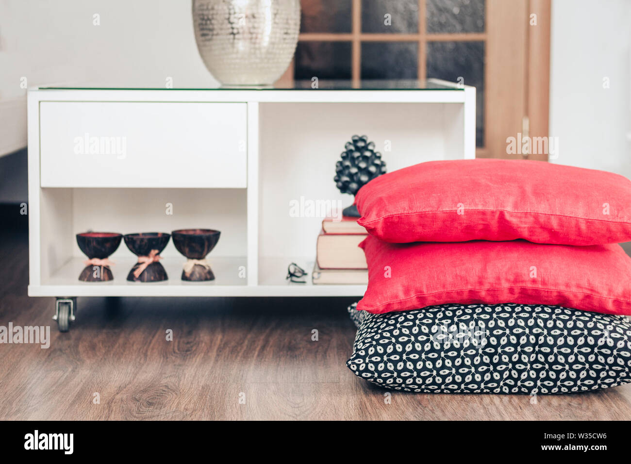 Cozy home interior decor, white nightstand with pile of books, candles in coconut shell with decorative pillows background Stock Photo