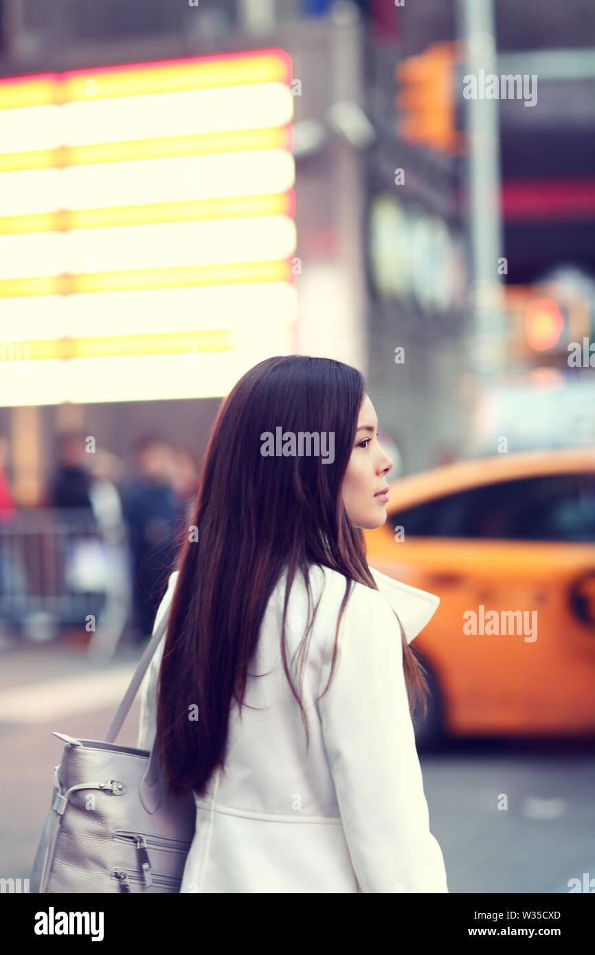 Woman in New York City Manhattan. Young urban professional business woman walking in street wearing coat downtown with yellow taxi cabs in background. Multiracial Asian Caucasian businesswoman in USA. Stock Photo