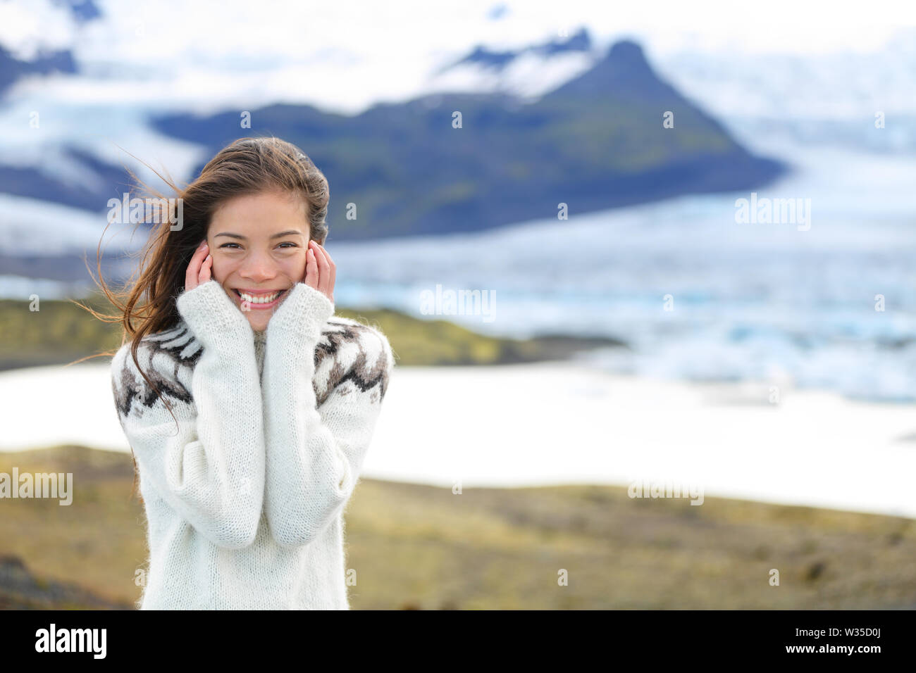 Asian woman portrait by glacier on Iceland wearing Icelandic sweater. Hiker tourist girl smiling cute in nature by glacial lagoon / lake of Fjallsarlon, Vatna glacier, Vatnajokull National Park. Stock Photo