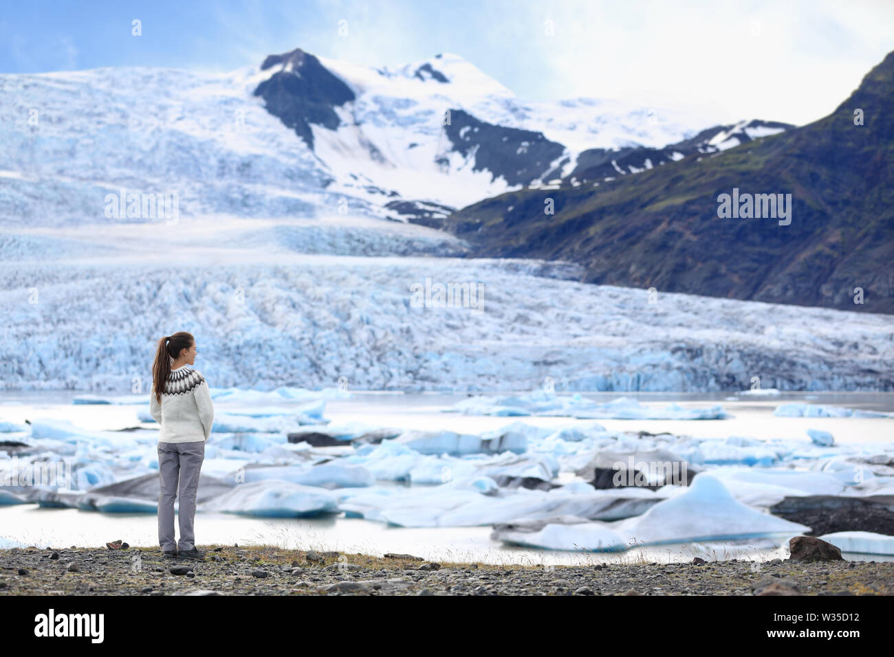 Adventure woman by glacier nature on Iceland. Tourist in Icelandic sweater by glacial lagoon / lake of Fjallsarlon, Vatna glacier, Vatnajokull National Park. Young woman visiting nature landscape. Stock Photo