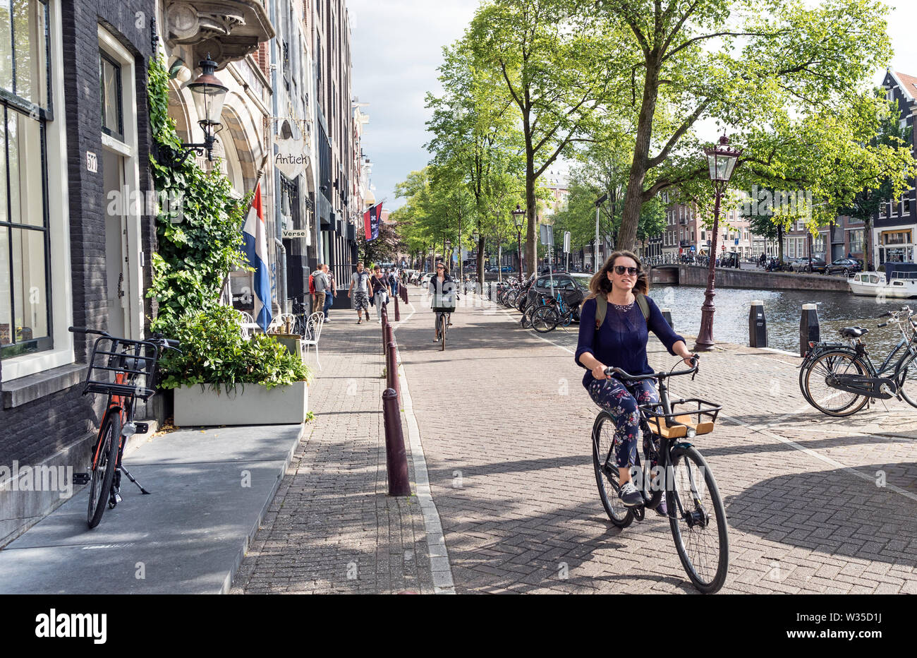 People Cycling By The Canals In Amsterdam Holland Stock Photo