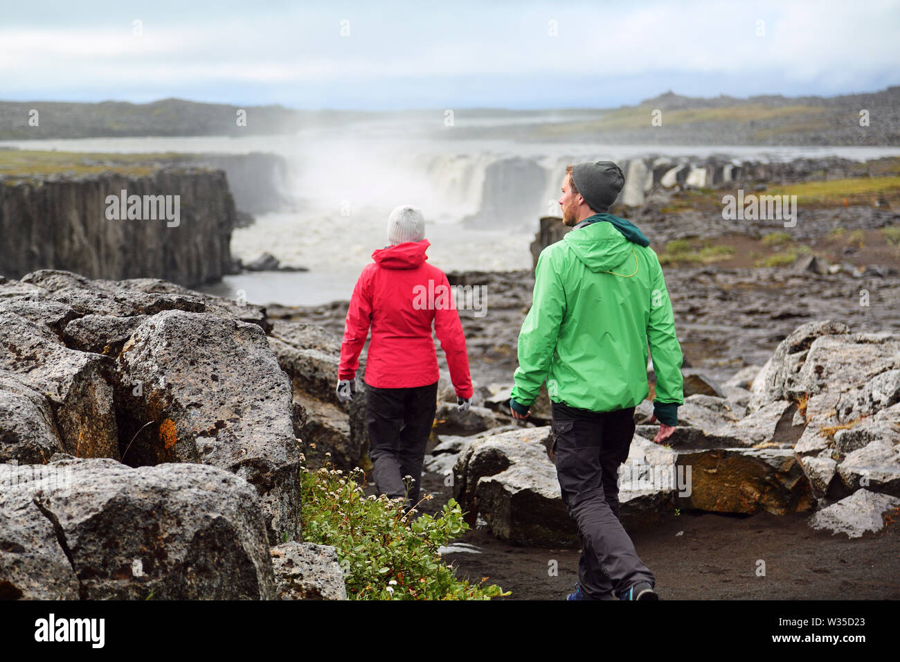 Hiking people in Iceland nature landscape with Selfoss waterfall. Hikers walking with view of famous Icelandic tourist attraction destination in Vatnajokull national park. Stock Photo