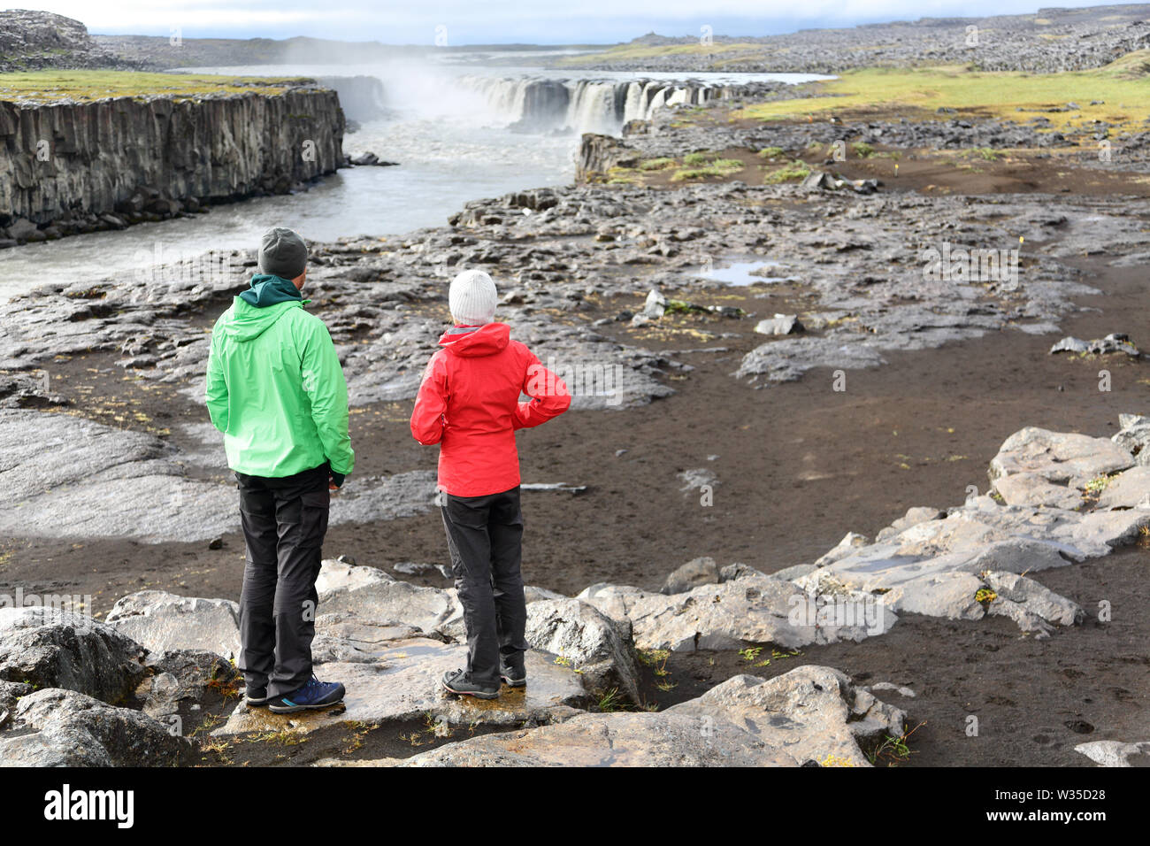 Iceland nature landscape with people by Selfoss waterfall. Hikers enjoying view of famous Icelandic tourist attraction destination. Hiking couple taking break by Selfoss in Vatnajokull national park. Stock Photo