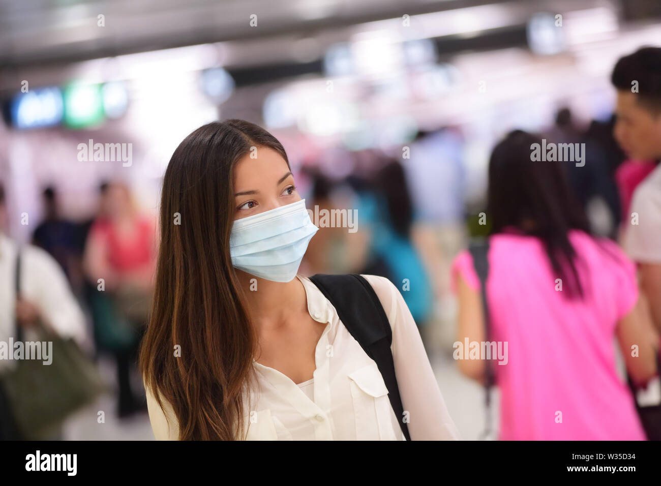 Person wearing protective mask against transmissible infectious diseases and as protection against pollution and the flu. Asian woman commuter in airport public area. Stock Photo