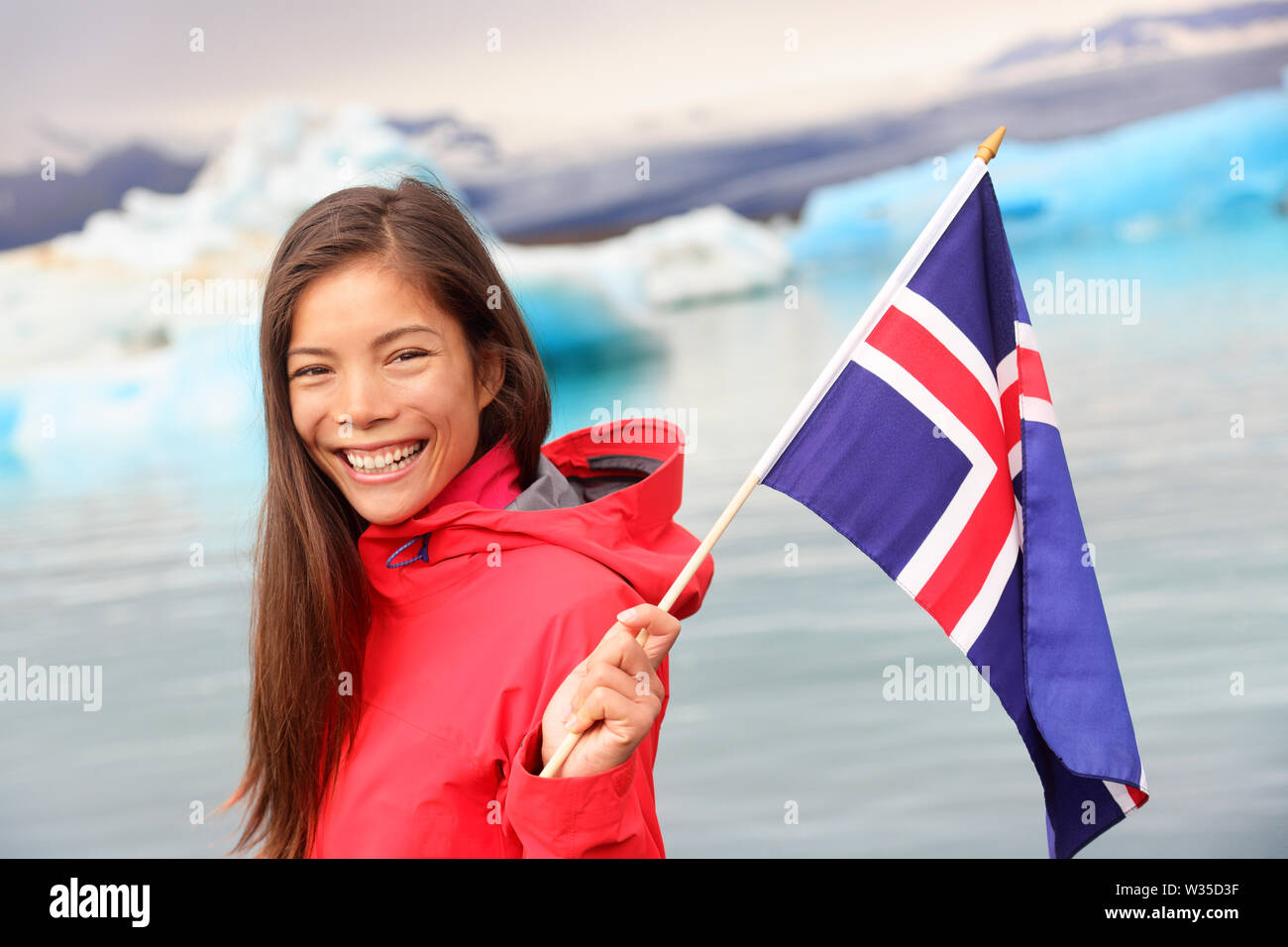 Icelandic flag - girl holding Iceland flag at glacier lagoon / glacial lake Jokulsarlon. Happy smiling woman tourist in front of iceberg. Stock Photo