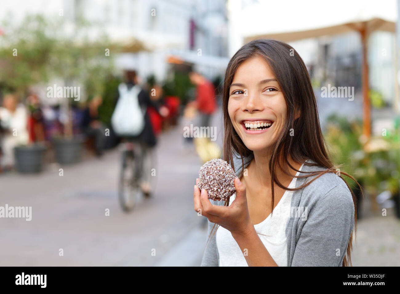 Woman eating traditional danish food floedeboller also called cream buns or marshmallow teacake. Girl enjoying the chocolate covered treat outside in city street of Copenhagen, Denmark. Stock Photo