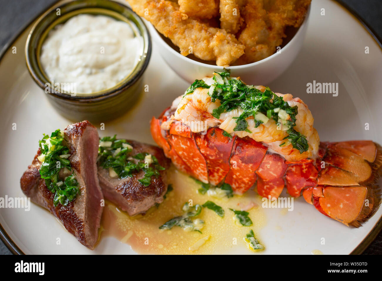 A homemade dish of surf and turf. It features a lobster tail that has been grilled, and a flash fried roe deer saddle fillet that have both had a garl Stock Photo