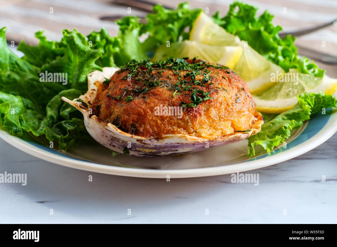 Stuffed seasoned clams garnished with romaine lettuce and lemon wedges on a marble kitchen table Stock Photo