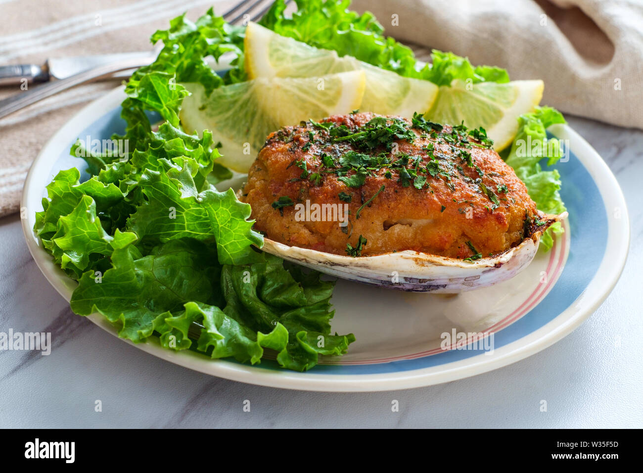 Stuffed seasoned clams garnished with romaine lettuce and lemon wedges on a marble kitchen table Stock Photo