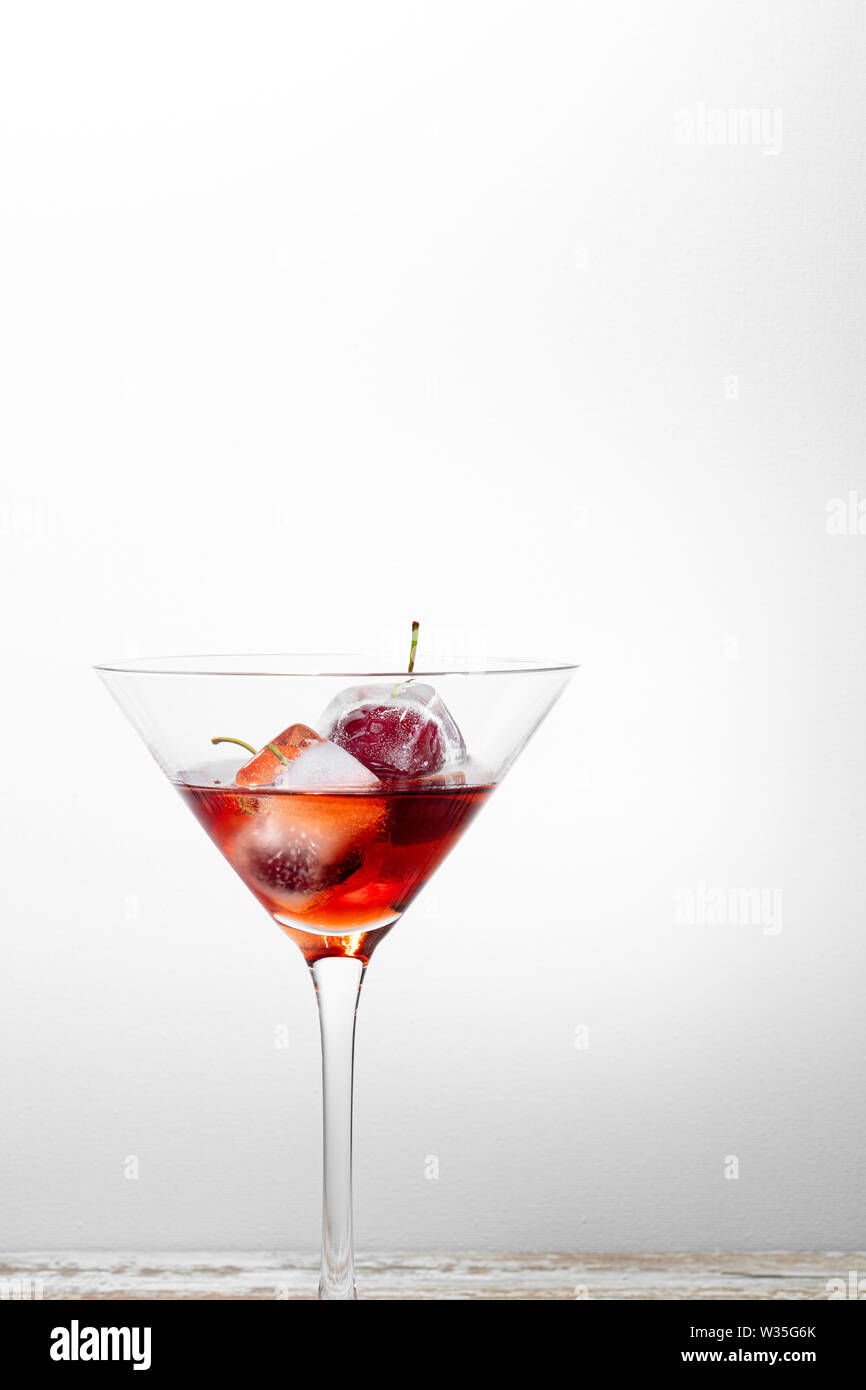 ice cubes with cherries inside into a red cocktail, white background textured with free space for text Stock Photo