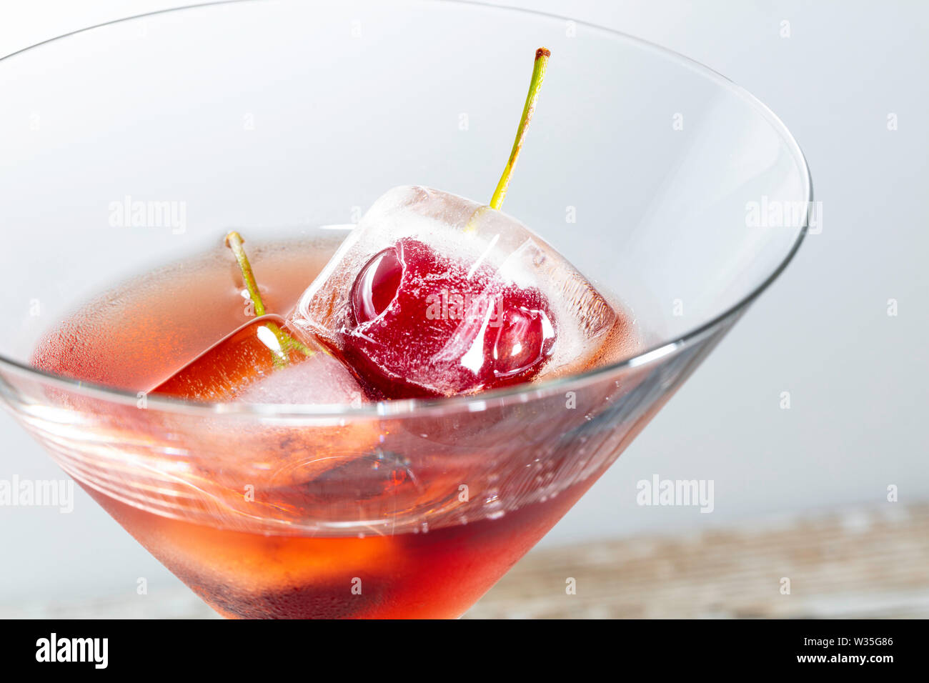 ice cubes with cherries inside into a red cocktail, white background with free space for text Stock Photo