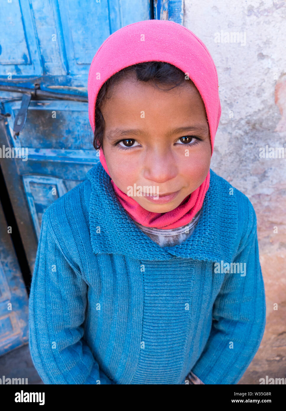 A Close Up of a Traditonal Little Berber Girl Looking Up at the Camera in the Traditional Berber Head Covering in a Village near Marrakresh in Morocco Stock Photo