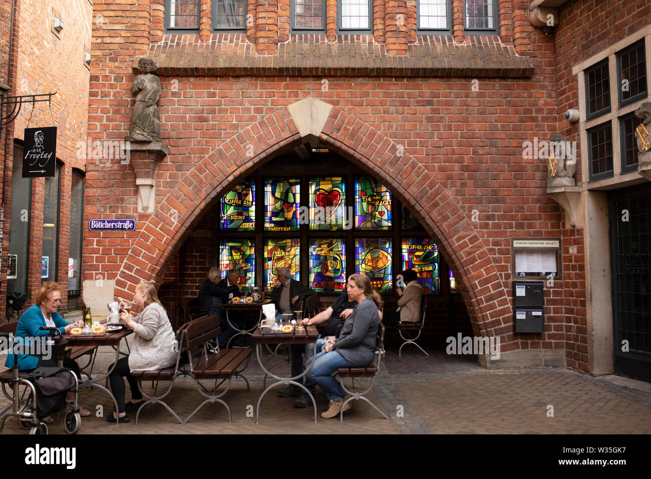 Stained glass windows and outdoor tables with people eating and drinking at Bar Freytag on Böttcherstrasse in central Bremen, Germany. Stock Photo